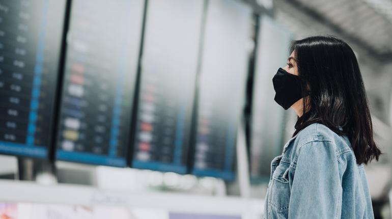 Asian woman traveler wearing mask protect from coronavirus looking flight information board display