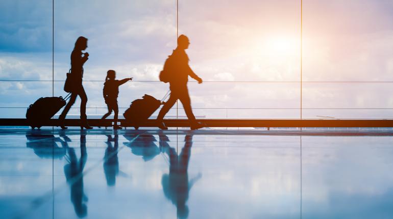 Family at airport travelling with young child and luggage walking to departure gate, girl pointing at airplanes through window, silhouette of people, abstract international air travel concept