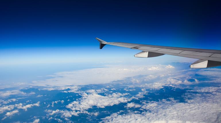 Wing of airplane over white clouds in sunny day.